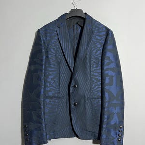 Puede incluir: Una chaqueta azul oscuro con un diseño estampado. La chaqueta tiene un cierre de un solo botón con dos botones y una solapa de muesca.