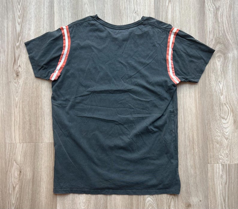 May include: A dark gray t-shirt with white and red stripes on the sleeves.