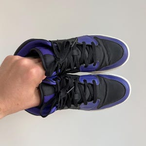 May include: A pair of black and purple high-top sneakers with white soles. The laces are black and the shoes have a padded tongue.