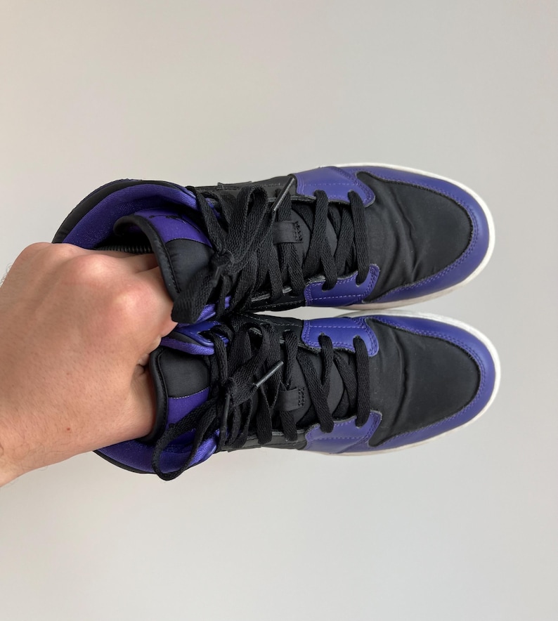 May include: A pair of black and purple high-top sneakers with white soles. The laces are black and the shoes have a padded tongue.