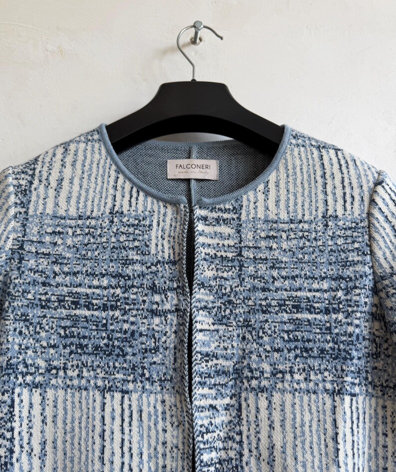May include: A long-sleeved knit jacket featuring a blue and white checkered pattern with a textured finish. The garment has a round neckline with a solid light blue trim and a front opening. A label inside the neck reads Falconeri made in Italy.