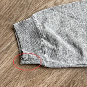 May include: Close-up of the grey ribbed cuff of a sweatshirt. The cuff is sewn with a seam that is slightly frayed.