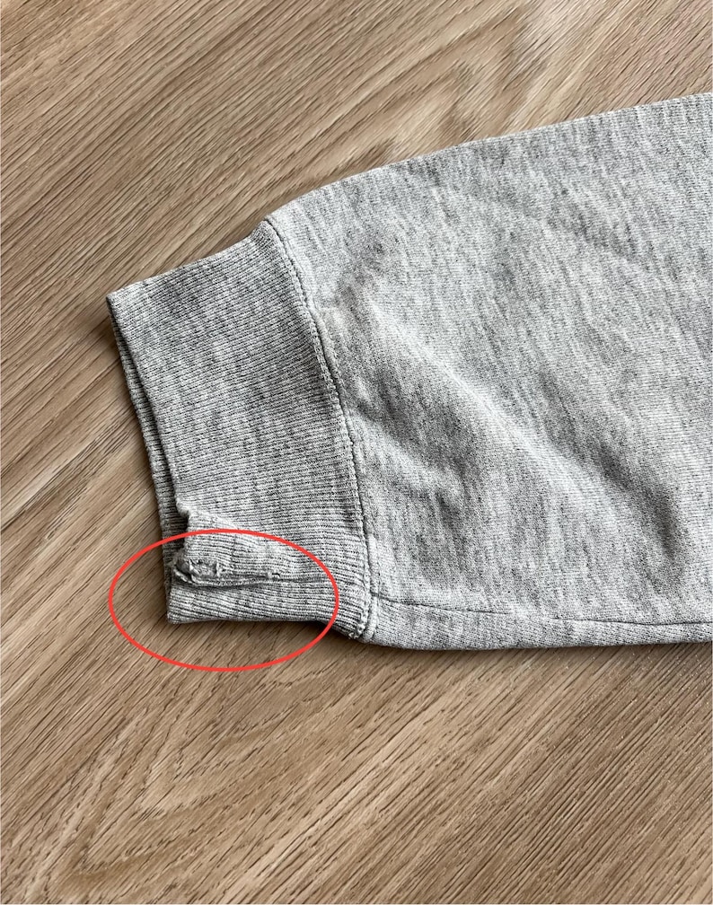 May include: Close-up of the grey ribbed cuff of a sweatshirt. The cuff is sewn with a seam that is slightly frayed.