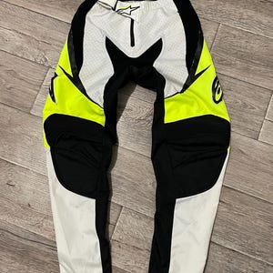 Puede incluir: Pantalón de motocross negro y blanco con detalles en amarillo neón. El pantalón tiene una cremallera y un cinturón. El pantalón tiene rodilleras y un asiento acolchado.