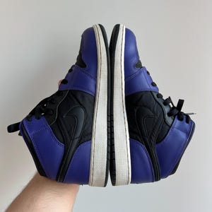 May include: A pair of black and purple high-top sneakers with a white sole. The sneakers have a black Nike swoosh logo on the side.