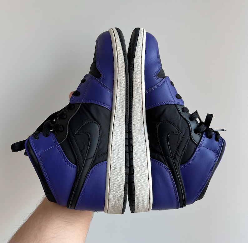 May include: A pair of black and purple high-top sneakers with a white sole. The sneakers have a black Nike swoosh logo on the side.