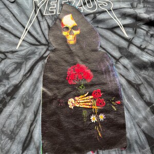 Może przedstawiać: Koszulka typu tie-dye z napisem "YEEZUS" w kolorze białym u g&oacute;ry. Koszulka przedstawia grafikę ponurego żniwiarza trzymającego czerwone r&oacute;że i stokrotki. Żniwiarz ma głowę czaszki i nosi czarny płaszcz.