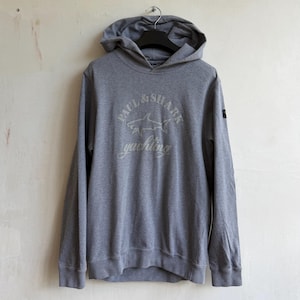 May include: A heather gray long-sleeve hooded sweatshirt featuring a large graphic on the chest with the text Paul & Shark Yachting and a shark illustration. The hoodie has a small dark patch on the left sleeve and a ribbed hem and cuffs.