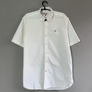 May include: A white short-sleeved button-down shirt with a small logo on the left chest. The logo is a black circle with a white ape head inside. The shirt has a button-down collar and a button placket.