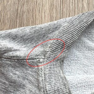 May include: Close-up of a grey sweatshirt with a small hole in the seam at the shoulder.
