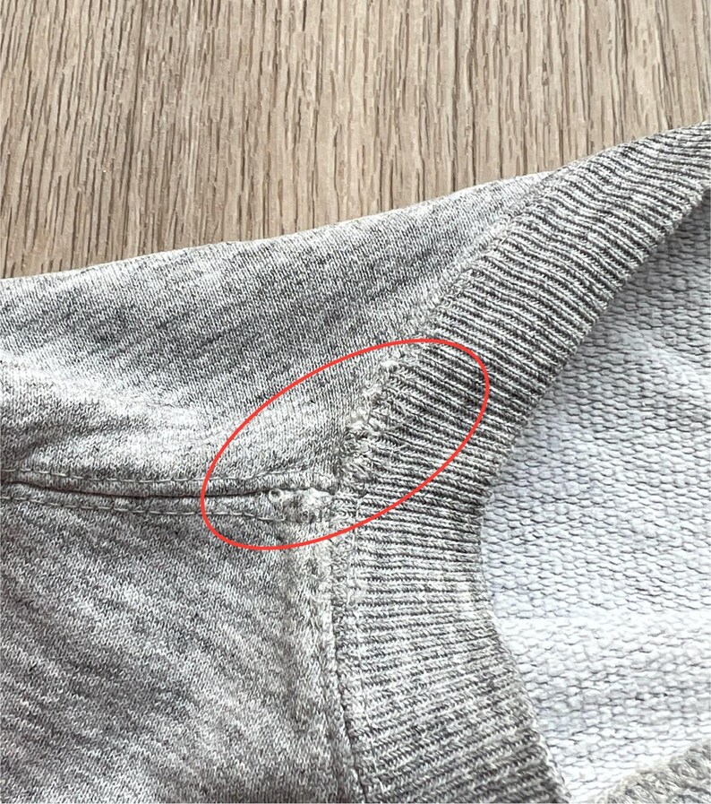 May include: Close-up of a grey sweatshirt with a small hole in the seam at the shoulder.