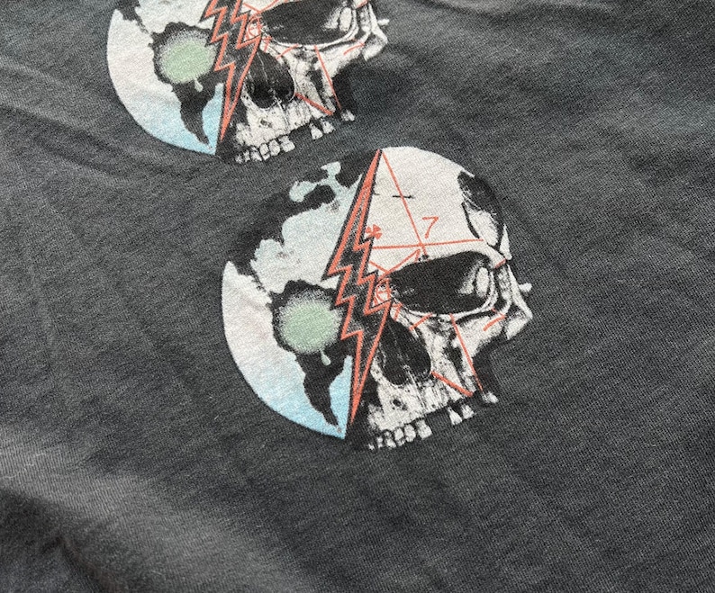 May include: Gray t-shirt with a graphic print of a skull with a lightning bolt and geometric patterns on a blue and green globe.