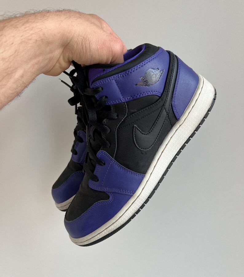 May include: Black and purple mid-top sneakers with a white sole and a Nike swoosh logo on the side.