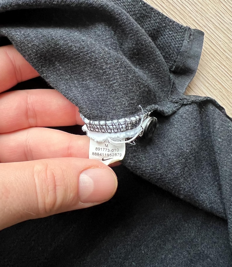May include: A black Nike tag with white text and a white swoosh logo. The tag reads "M 891773-010 888411952879".