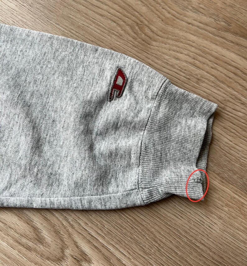 May include: Grey sweatshirt with a red and white logo on the sleeve. The sleeve has a ribbed cuff.