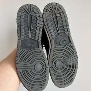 May include: A pair of black Nike sneakers with white soles and a black and white tread pattern. The sneakers have the Nike logo on the back of the heel.