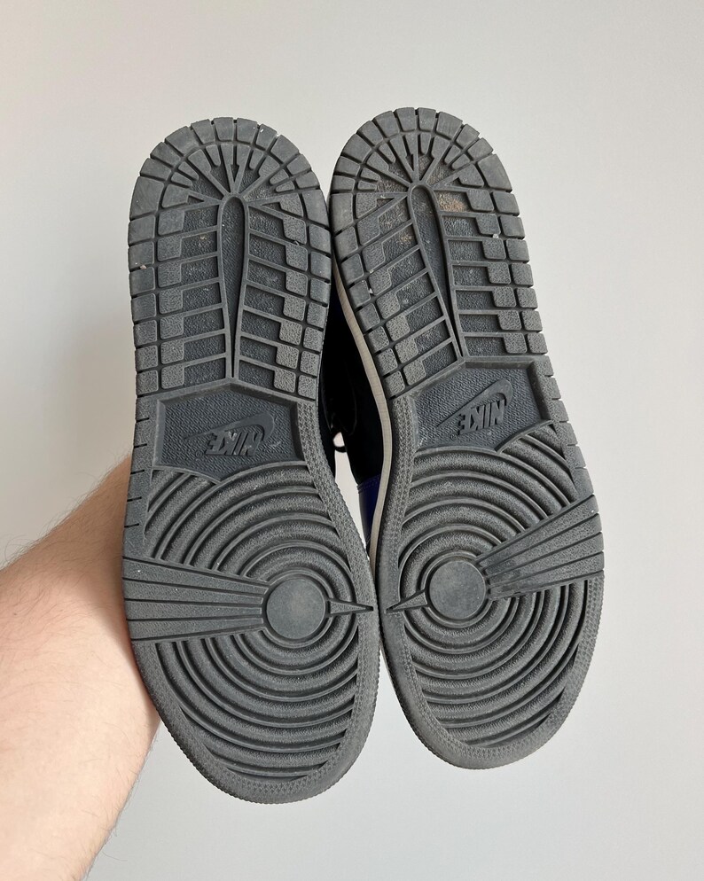 May include: A pair of black Nike sneakers with white soles and a black and white tread pattern. The sneakers have the Nike logo on the back of the heel.