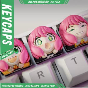 Könnte beinhalten: Nahaufnahme von drei individuellen Resin-Tastenkappen mit einem pinkhaarigen Anime-Charakter mit großen grünen Augen. Die Tastenkappen befinden sich auf einer weißen Tastatur, wobei die Buchstaben "R" und "T" sichtbar sind. Der Text "KEYCAPS" und "MAY 2025 COLLECTION" sind ebenfalls sichtbar.