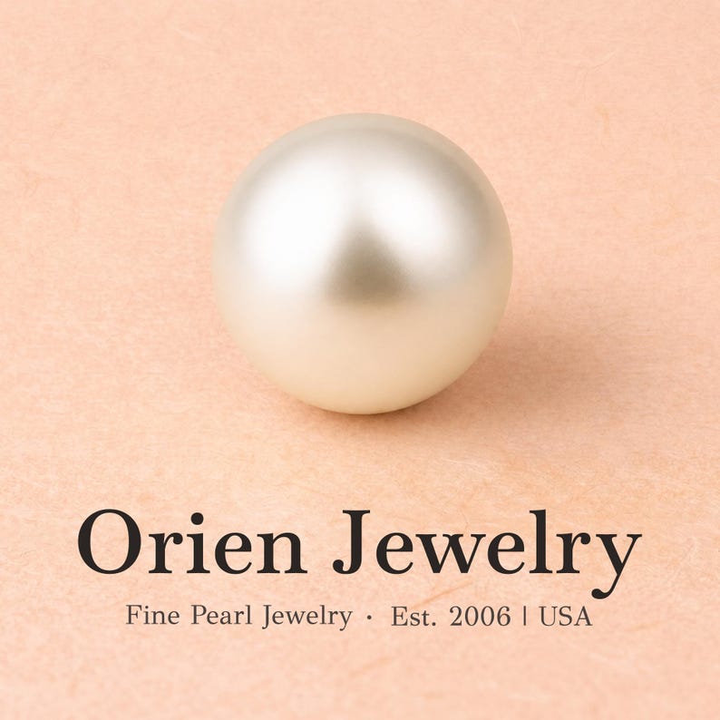 May include: A single, smooth, spherical white pearl with a soft luster. Below the pearl, the text reads: Orien Jewelry, Fine Pearl Jewelry &middot; Est. 2006 | USA. The pearl is centered above the black text, which is printed on a light peach-colored background.