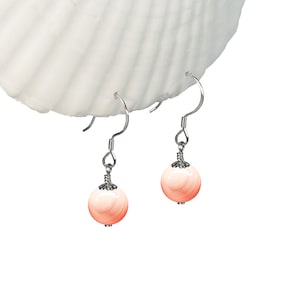 May include: A pair of silver dangle earrings with pink and white shell bead drops.