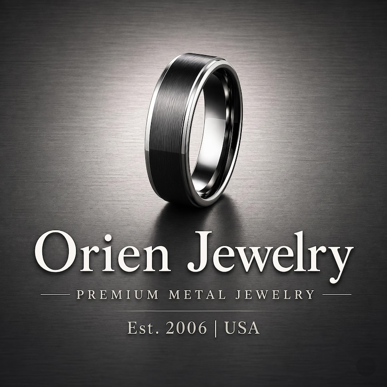 May include: A black ring with a brushed metal finish and a silver-colored inner band. The ring is displayed on a dark gray surface. The text "Orien Jewelry" is displayed in white, along with "Premium Metal Jewelry" and "Est. 2006 | USA".