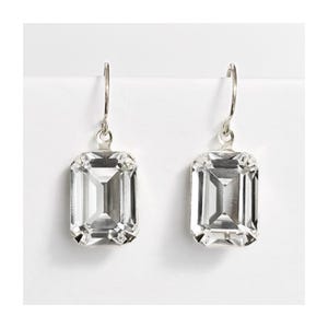 May include: A pair of silver dangle earrings with clear emerald-cut crystal stones.