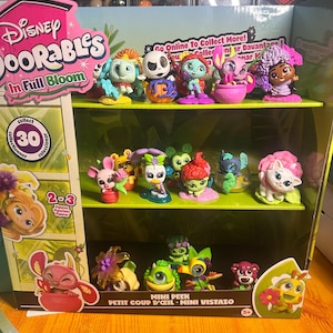 Puede incluir: Una vitrina llena de figuras de Disney Doorables. La vitrina presenta múltiples estantes que contienen varias figuras coloridas, incluidos personajes de películas de Disney. El embalaje dice "Disney Doorables In Full Bloom" y "Mini Peek".