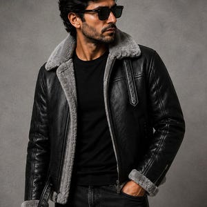 May include: A black leather jacket with a grey faux fur lining, a wide collar, and a front zipper closure. The jacket features long sleeves with grey faux fur cuffs, a buckled strap at the hem, and a vertical strap detail on the chest area.
