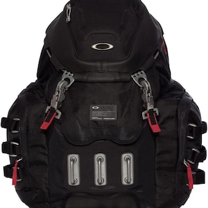 May include: A black backpack featuring a structured top compartment with a silver Oakley logo, metallic side-release buckles with red accents, three vertical silver hardware loops on the front, and a small rectangular patch with white text.