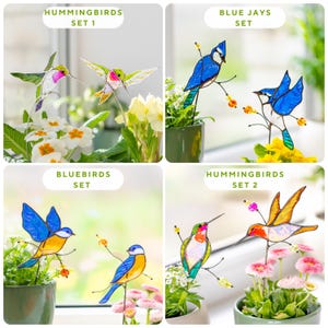 May include: Four sets of colourful stained glass bird ornaments, including hummingbirds, blue jays, and bluebirds, are displayed in small green pots with flowers. The birds are perched on metal stems. Text on the image reads "HUMMINGBIRDS SET 1", "BLUE JAYS SET", "BLUEBIRDS SET", and "HUMMINGBIRDS SET 2".