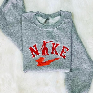 Puede incluir: Sudadera gris con un logotipo de Nike rojo y la palabra "NIKE" en letras rojas.