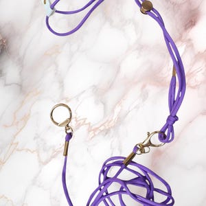 May include: Purple adjustable pet harness with a matching leash and gold hardware. The harness has two adjustable straps and a clip on the back. The leash has a gold ring and a clip on the end.
