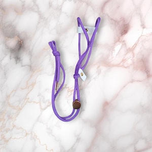 May include: A purple and white phone strap with a leather accent and gold hardware. The strap is made of two cords that are tied together at the top.