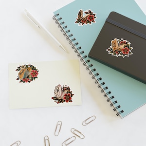 May include: Four die-cut stickers featuring illustrations of lizards, including a bearded dragon and a gecko, each surrounded by red flowers and green leaves. The stickers are placed on a light blue spiral notebook, a dark gray journal, and a cream card.