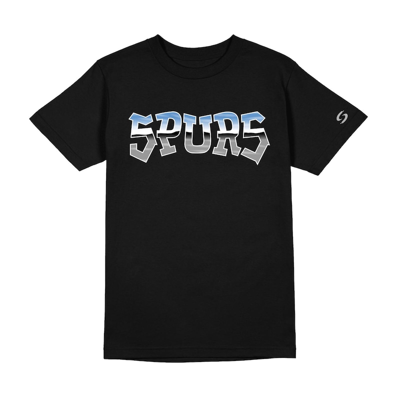 May include: A black short-sleeved t-shirt featuring the word SPURS printed across the chest in a metallic-style font with a blue and silver gradient. A small silver logo is visible on the left sleeve near the shoulder seam.