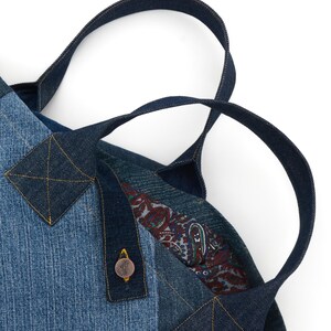 May include: A blue denim tote bag with a paisley lining and a button closure. The bag has two handles made of denim.
