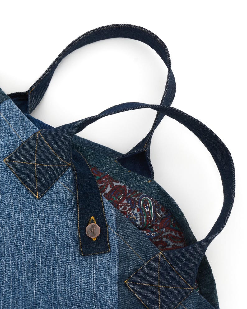 May include: A blue denim tote bag with a paisley lining and a button closure. The bag has two handles made of denim.