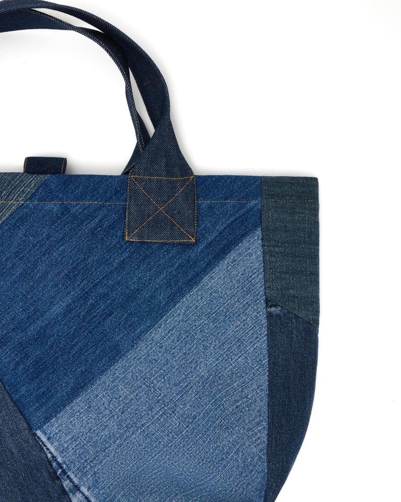 May include: A blue denim tote bag made from patchwork fabric. The bag has a single top handle and a rectangular shape.