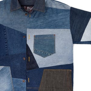 Puede incluir: Una camisa vaquera azul hecha de diferentes tonos de tejido vaquero. La camisa tiene un cierre de botones en la parte delantera, un cuello y un bolsillo de parche en el pecho izquierdo. La camisa est&aacute; hecha de un mosaico de diferentes tejidos vaqueros.