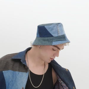 Op de afbeelding: Een blauwe denim bucket hat gemaakt van patchwork stof. De hoed heeft een brede rand en een platte kroon.