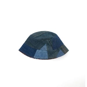 May include: A blue denim bucket hat made from patchwork fabric. The hat is made from different shades of blue denim and has a slightly curved brim.