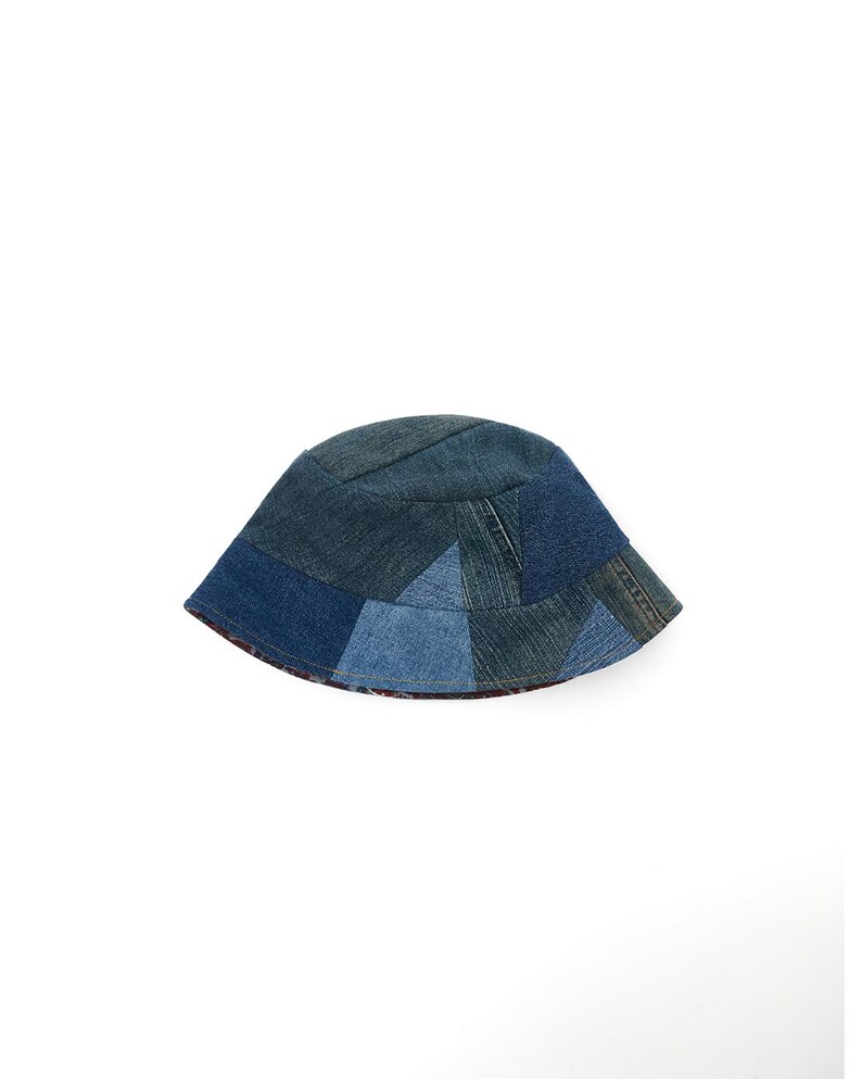 May include: A blue denim bucket hat made from patchwork fabric. The hat is made from different shades of blue denim and has a slightly curved brim.