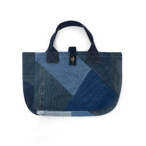 May include: A blue denim tote bag made from patchwork fabric. The bag has a single top handle and a button closure.