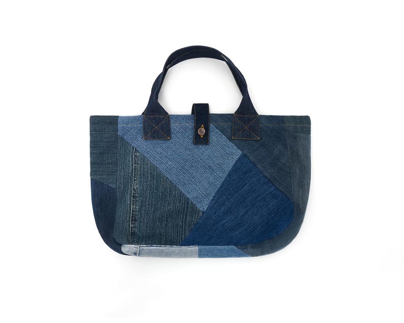 May include: A blue denim tote bag made from patchwork fabric. The bag has a single top handle and a button closure.