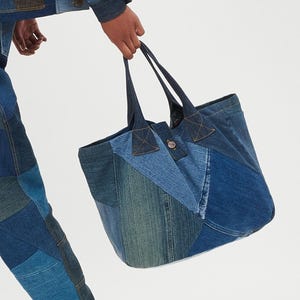 May include: A large blue denim tote bag made from patchwork denim fabric. The bag has two long handles and a button closure.