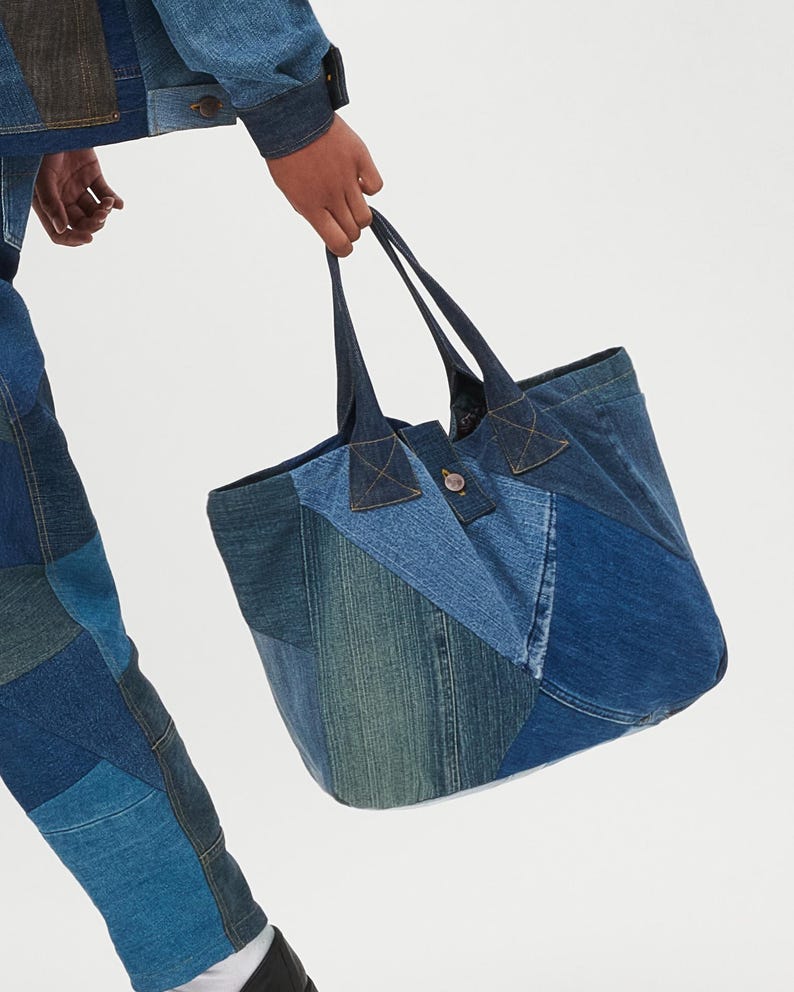 May include: A large blue denim tote bag made from patchwork denim fabric. The bag has two long handles and a button closure.