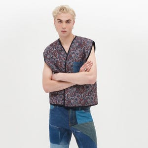 Puede incluir: Un chaleco sin mangas con un estampado paisley en tonos azules, rojos y blancos. El chaleco tiene un bolsillo de parche de mezclilla en la parte delantera. El modelo lleva pantalones vaqueros de mezclilla con parches azules.
