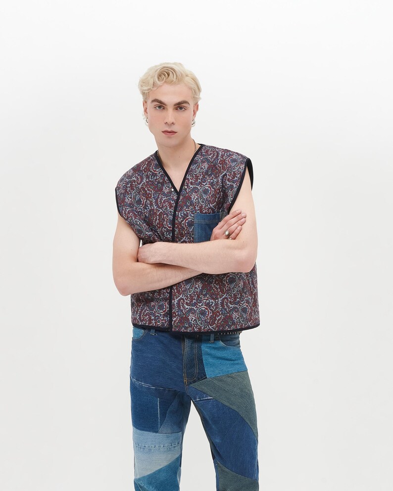 Puede incluir: Un chaleco sin mangas con un estampado paisley en tonos azules, rojos y blancos. El chaleco tiene un bolsillo de parche de mezclilla en la parte delantera. El modelo lleva pantalones vaqueros de mezclilla con parches azules.