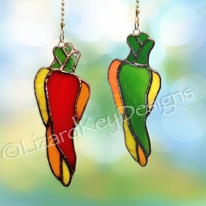 May include: Two stained glass chili pepper ornaments, one red and one green, with yellow and orange accents. The ornaments are hanging from a chain.