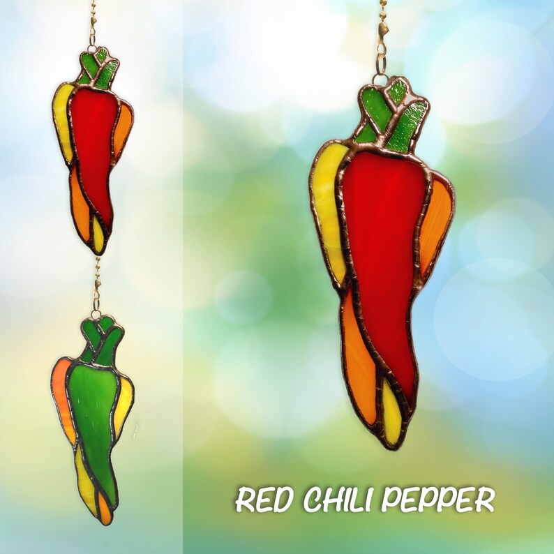 May include: A stained glass red chili pepper hanging ornament with yellow and green accents. The ornament is suspended from a gold chain.